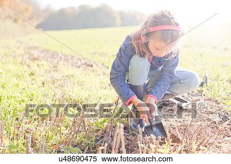 Stock Photography - Girl with metal detector crouching and digging with spade in field. Fotosearch