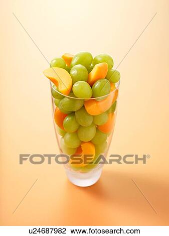 Stock Image - Glass full of grapes and apricot slices on light orange background. Fotosearch