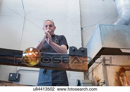 Stock Image - Glassblower blowing hot glass. Fotosearch