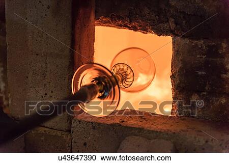 Stock Image - Glassblower heating glass in furnace. Fotosearch