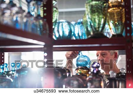 Stock Image - Glassblower inspecting finished glassware. Fotosearch