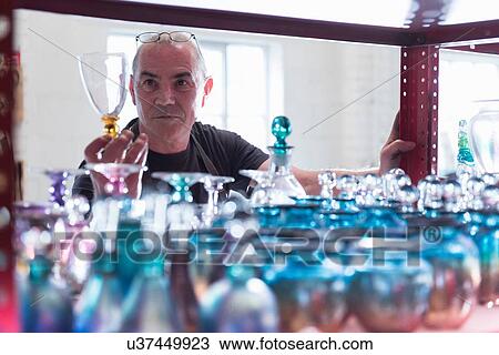 Stock Image - Glassblower inspecting finished glassware. Fotosearch
