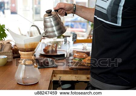 Stock Photo - Hand of cafe waiter pouring boiling water into filter coffee pot. Fotosearch