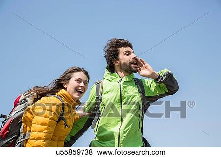 Stock Photo - Hiking couple against blue sky laughing and shouting. Fotosearch
