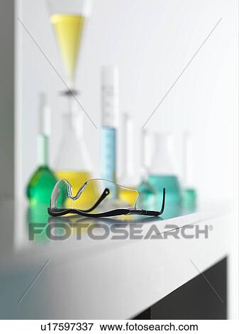Stock Photo - Laboratory safety glasses on lab bench with a chemical experiment in background. Fotosearch
