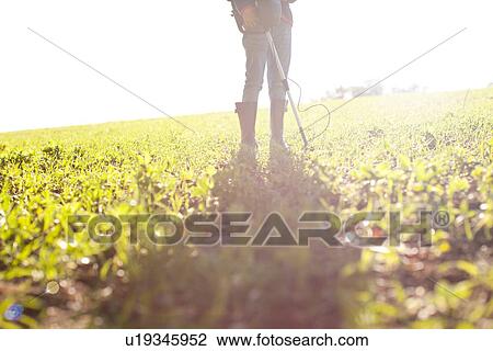 Stock Image - Legs of girl using metal detector in field. Fotosearch