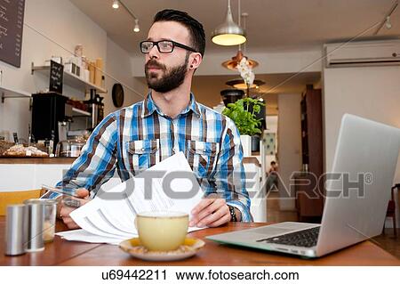 Male customer reading paperwork and using laptop at cafe table View Large Photo Image Stock Image - Male customer reading paperwork and using laptop at cafe table. Fotosearch