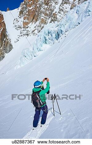 Stock Photo - Male skier taking smartphone photograph on Mont Blanc massif, Graian Alps, France. Fotosearch