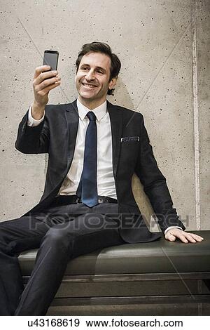 Stock Photo - Mature businessman, looking at smartphone, smiling. Fotosearch