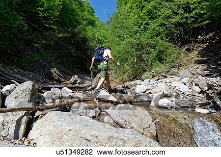 Stock Image - Mature male hiker crossing river. Fotosearch