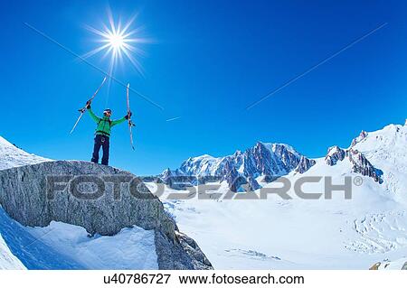 Stock Photo - Mature male skier holding up ski's on Mont Blanc massif, Graian Alps, France. Fotosearch