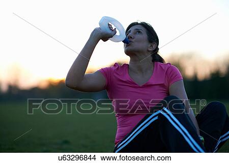 Mature woman taking a break from exercise and drinking water in park View Large Photo Image Picture - Mature woman taking a break from exercise and drinking water in park. Fotosearch
