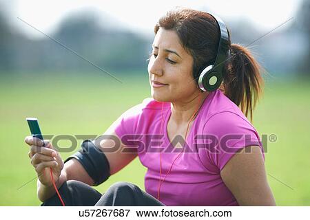 Stock Photo - Mature woman taking exercise break in park selecting music from MP3 player. Fotosearch