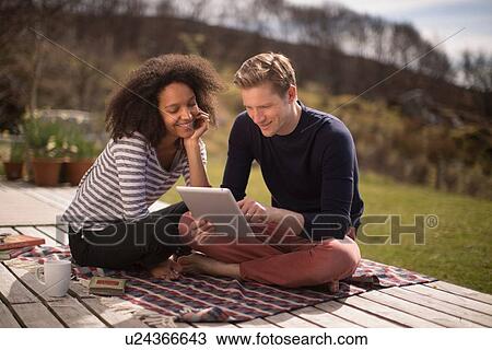 Mid adult couple sitting on blanket using tablet View Large Photo Image Stock Image - Mid adult couple sitting on blanket using tablet. Fotosearch