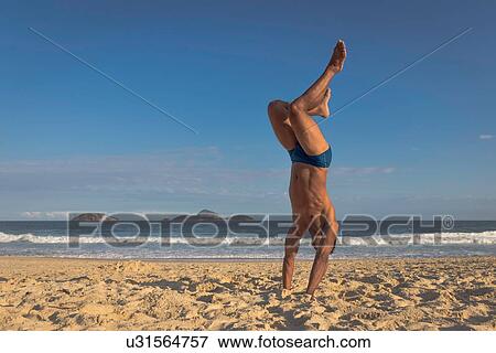 Stock Photo - Mid adult man doing handstand on beach, Rio de Janeiro, Brazil. Fotosearch