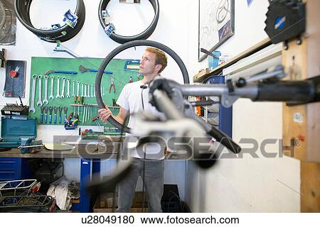 Mid adult man in repair shop holding bicycle tyre View Large Photo Image Stock Image - Mid adult man in repair shop holding bicycle tyre. Fotosearch