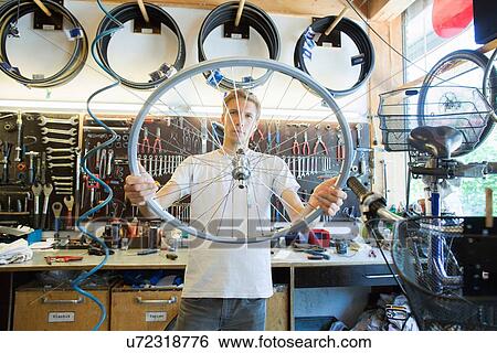 Stock Photograph - Mid adult man in repair shop looking through bicycle wheel. Fotosearch