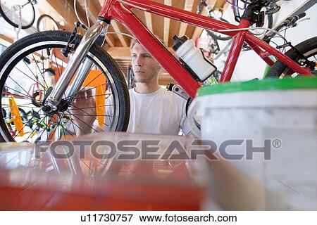 Stock Photo - Mid adult man in repair shop, view through bicycle frame. Fotosearch