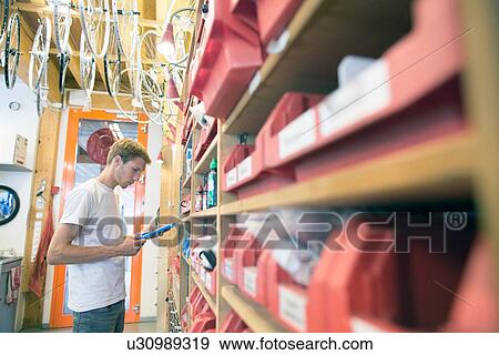 Stock Photo - Mid adult man in storage room choosing bicycle part. Fotosearch