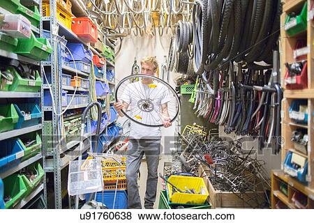 Stock Photo - Mid adult man in storage room holding bicycle wheel. Fotosearch