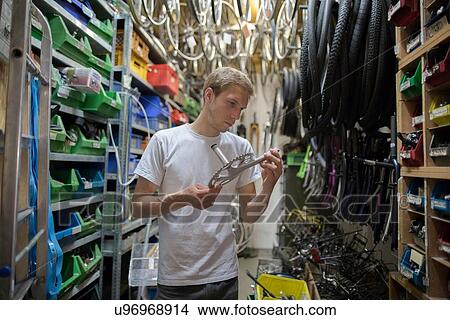 Mid adult man in storage room looking at bicycle part View Large Photo Image Picture - Mid adult man in storage room looking at bicycle part. Fotosearch