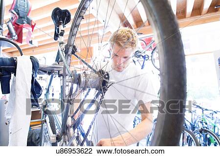 Stock Image - Mid adult man repairing bicycle, view through wheel. Fotosearch