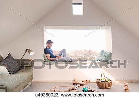 Mid adult man sitting in window seat, reading View Large Photo Image Stock Image - Mid adult man sitting in window seat, reading. Fotosearch