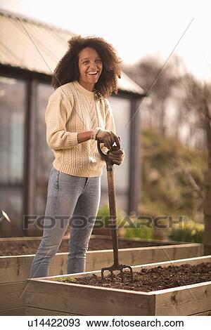 Stock Image - Mid adult woman by raised bed with garden fork, portrait. Fotosearch