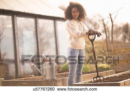 Stock Image - Mid adult woman by raised bed with garden fork, portrait. Fotosearch
