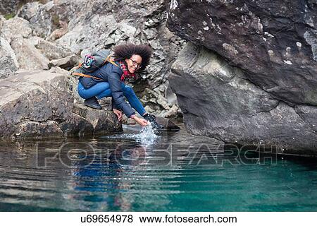 Stock Photo - Mid adult woman crouching by pond. Fotosearch