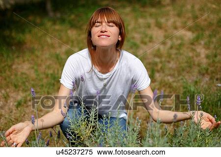 Stock Photography - Mid adult woman crouching smelling lavender, eyes closed, arms open. Fotosearch