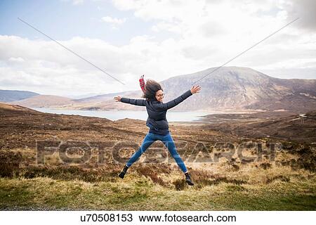 Stock Image - Mid adult woman in mountains doing star jump, Isle of Skye, Hebrides, Scotland. Fotosearch