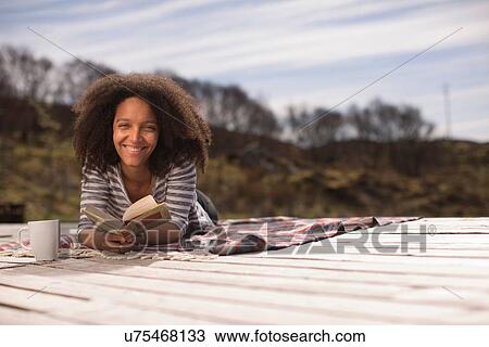 Mid adult woman lying down holding book, portrait View Large Photo Image Stock Image - Mid adult woman lying down holding book, portrait. Fotosearch