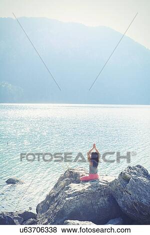 Mid adult woman, sitting on rock, beside lake, in yoga position, rear view View Large Photo Image Stock Photo - Mid adult woman, sitting on rock, beside lake, in yoga position, rear view. Fotosearch