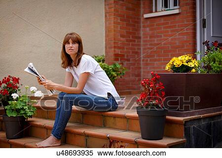 Stock Photography - Mid adult woman sitting outdoors holding newspaper, looking at camera. Fotosearch