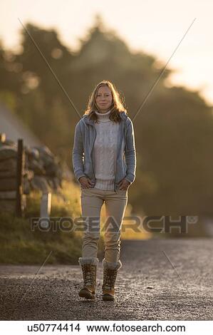 Picture - Mid adult woman walking along road. Fotosearch