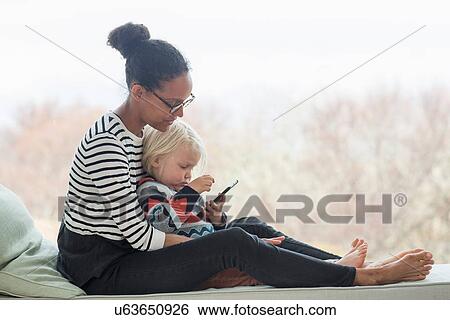 Mother and son sitting together using tablet View Large Photo Image Stock Photograph - Mother and son sitting together using tablet. Fotosearch