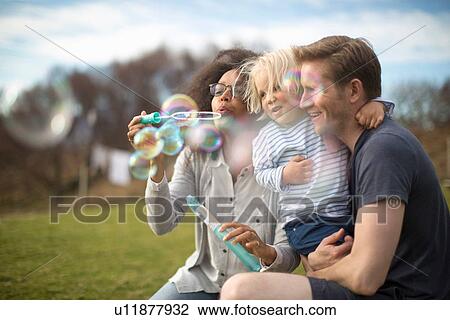 Stock Image - Mother blowing bubbles, father holding son. Fotosearch