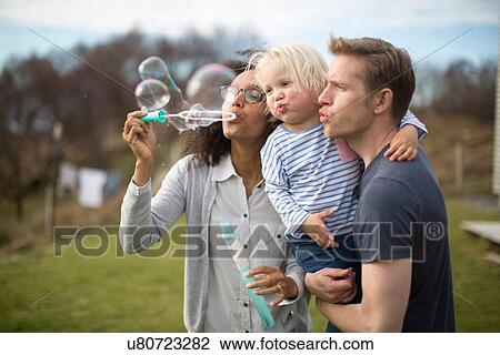 Mother blowing bubbles, father holding son View Large Photo Image Stock Image - Mother blowing bubbles, father holding son. Fotosearch