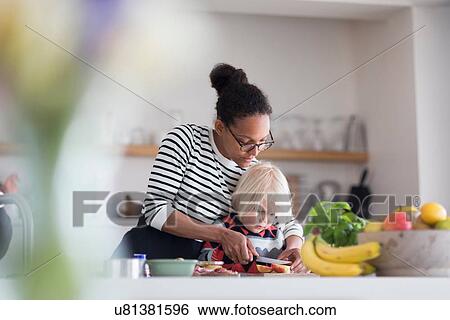 Stock Photograph - Mother helping son prepare food in kitchen. Fotosearch