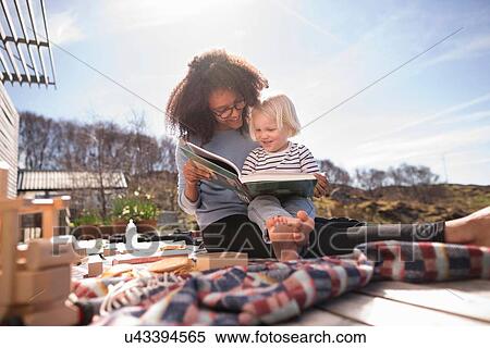 Stock Photography - Mother reading book to son on picnic blanket. Fotosearch