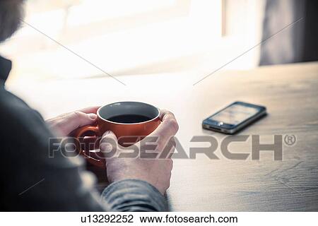 Over shoulder view of man drinking coffee with smartphone on desk View Large Photo Image Stock Image - Over shoulder view of man drinking coffee with smartphone on desk. Fotosearch