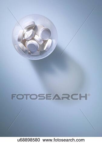 Stock Image - Overhead view of white tablets in plastic measuring cup. Fotosearch