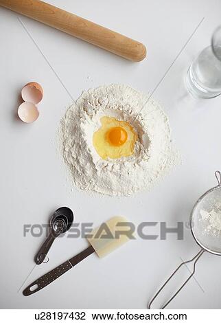 Stock Image - Overhead view with raw egg in center of flour stack and kitchen utensils. Fotosearch