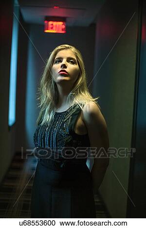 Stock Image - Portrait of beautiful blond young woman looking up in dark hotel corridor. Fotosearch