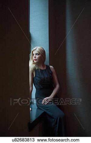 Stock Image - Portrait of beautiful blond young woman looking through hotel window. Fotosearch