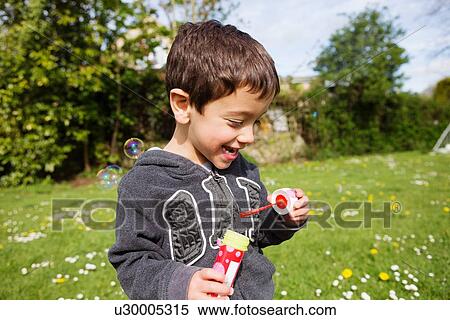 Stock Photography - Portrait of boy blowing bubbles in garden. Fotosearch