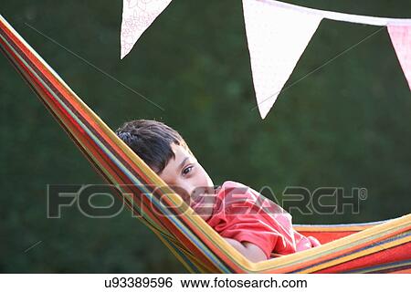 Stock Photograph - Portrait of cute boy reclining in striped garden hammock. Fotosearch
