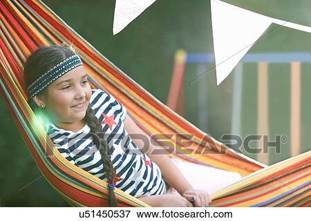 Stock Photo - Portrait of cute girl with hairband and plait reclining in striped garden hammock. Fotosearch