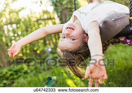 Stock Image - Portrait of girl leaning back upside down in garden. Fotosearch